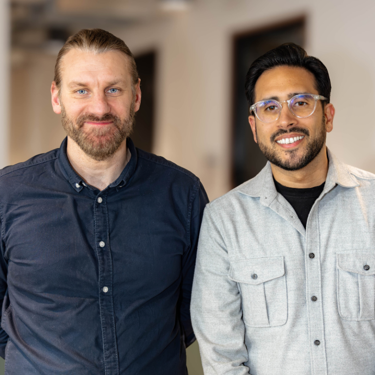 Two professional men smiling in a modern office setting for a "Meet the Team" page.